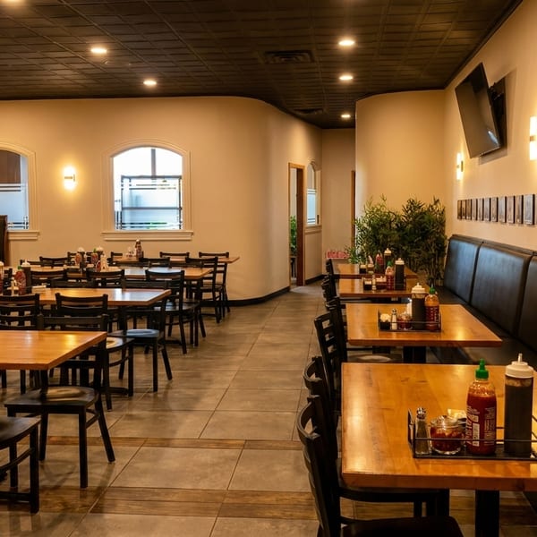Spacious restaurant dining room with wooden tables, black chairs, booths, and wall art under warm lighting.