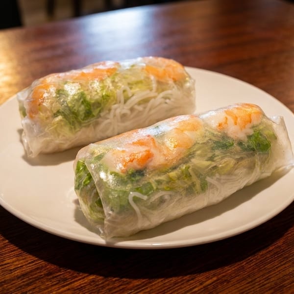 Two shrimp and vegetable spring rolls on a white plate atop a wooden table.