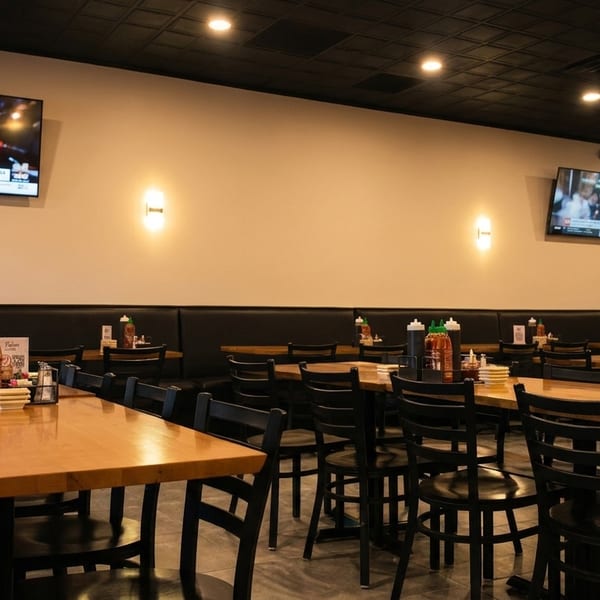 Empty restaurant dining room with wooden tables, black chairs, booth seating, and wall-mounted TVs.