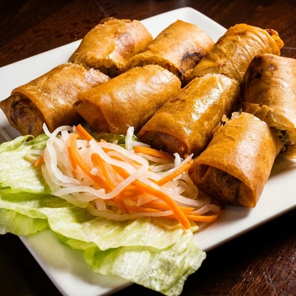 A plate of crispy golden spring rolls with fresh lettuce and pickled carrots and daikon.