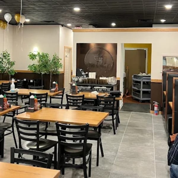 Empty restaurant dining room with wooden tables, black chairs, and a dark brown accent wall.